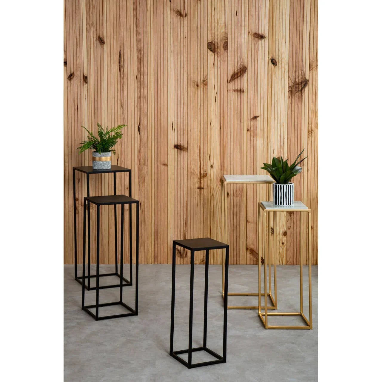 Set of black and gold metal side tables with plants on grey floor and wooden wall background