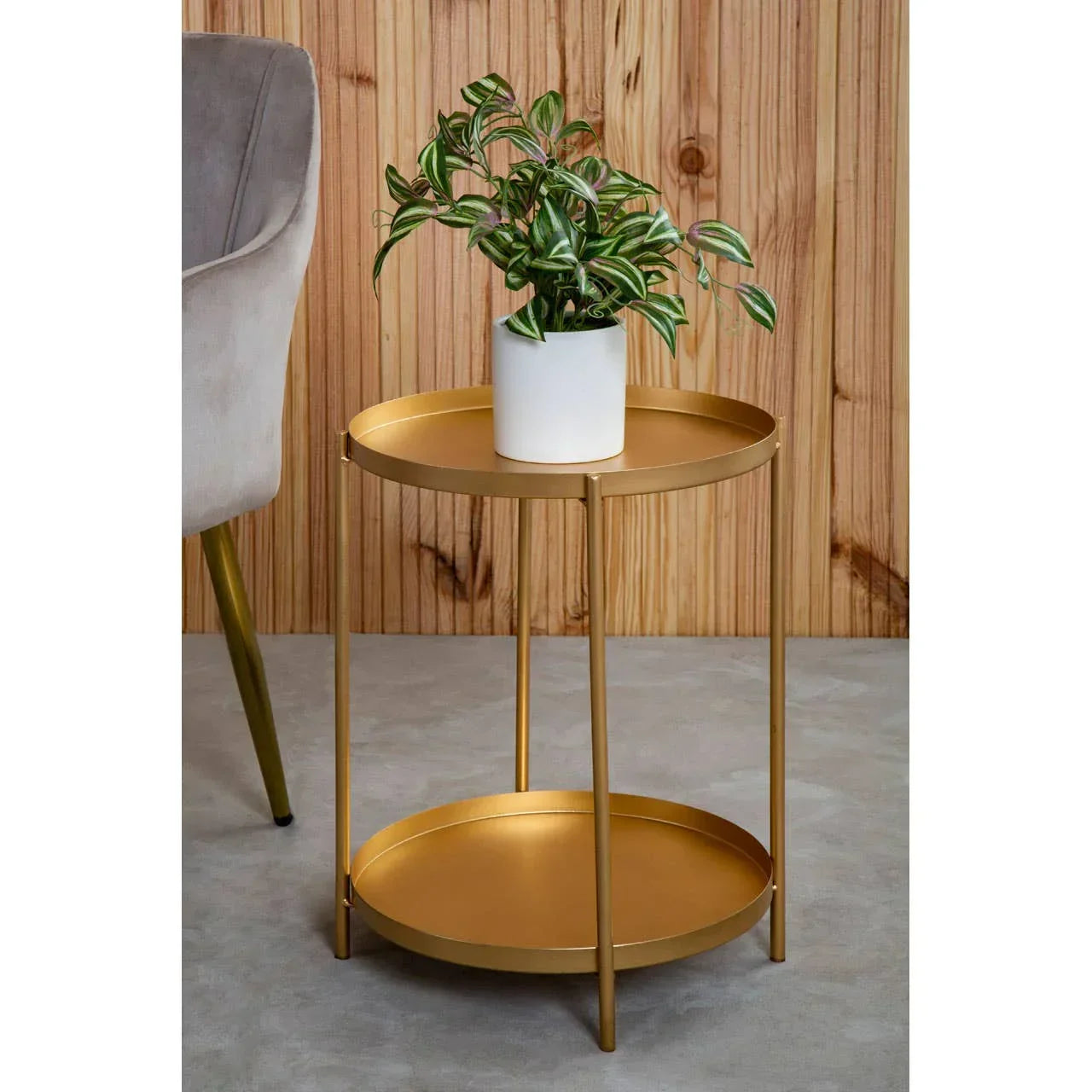 Gold metal side table with round tray shelves and potted plant, set on a grey floor