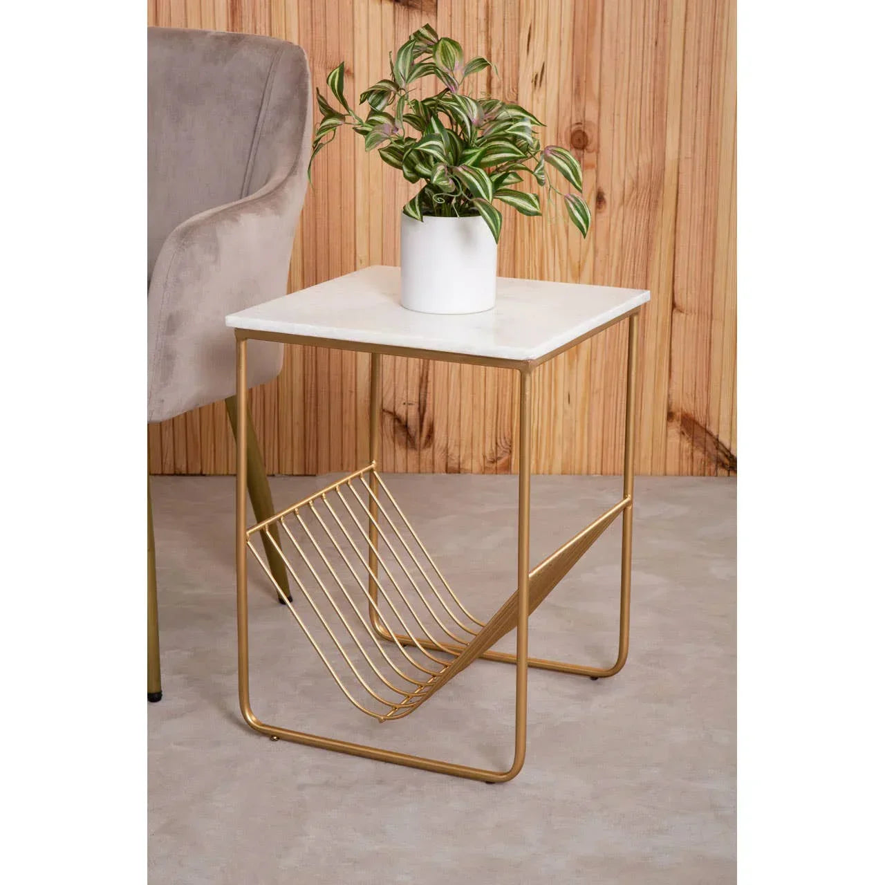 Gold metal side table with marble top and magazine rack, potted plant on top, indoors