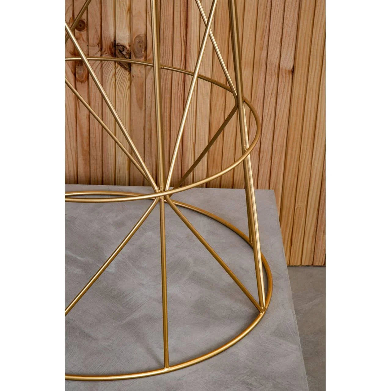 Gold metal table base with geometric design on concrete floor, wood panel background