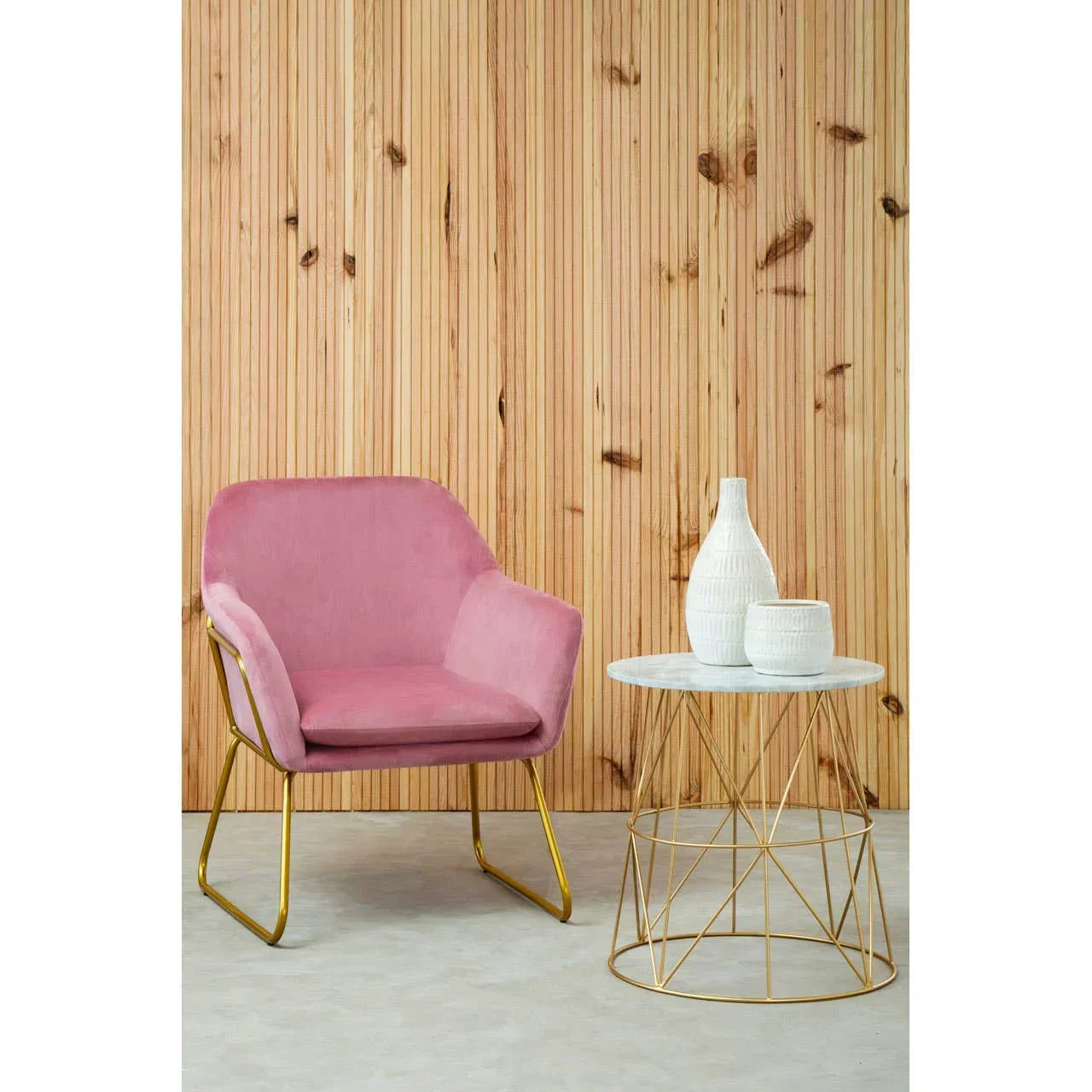 Pink velvet accent chair with gold legs beside marble top side table and decorative vases