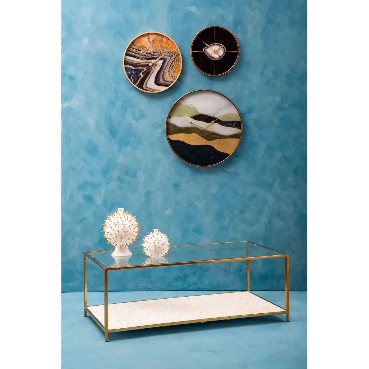 Glass coffee table with gold frame, two decorative vases, and abstract wall art on blue wall