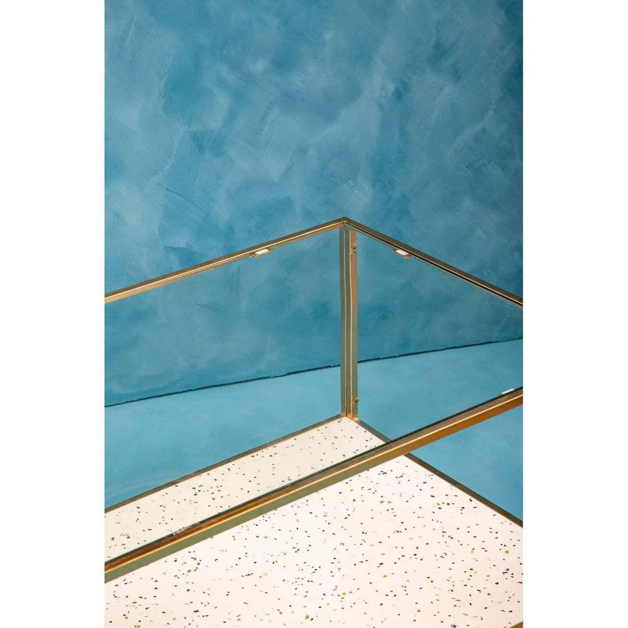 Glass and brass furniture corner with terrazzo top against blue wall