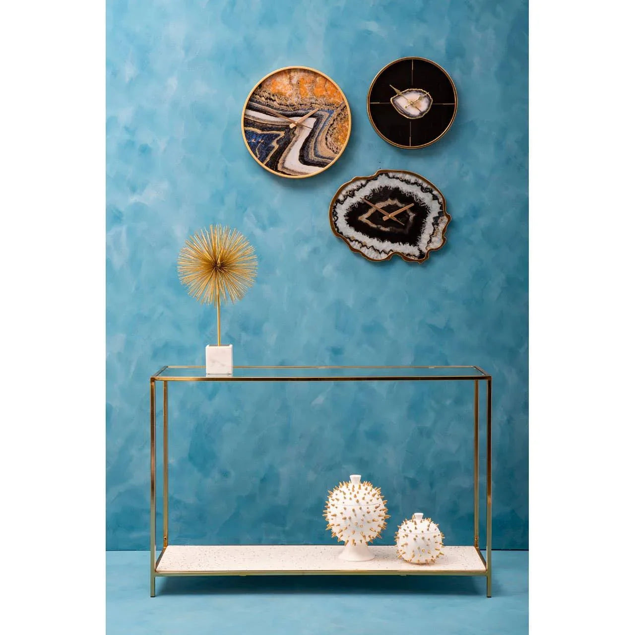 Gold console table with marble top, decorative ornaments, and abstract wall art on blue wall