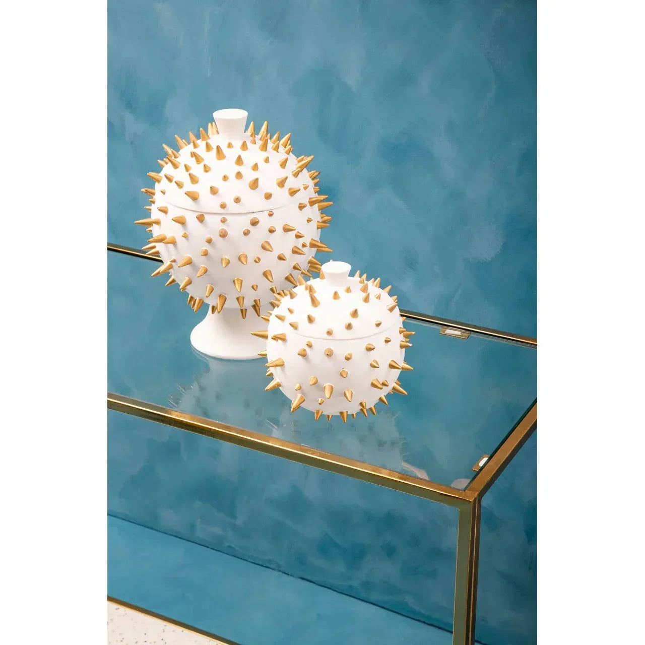 White ceramic decorative jars with gold spikes on glass console table