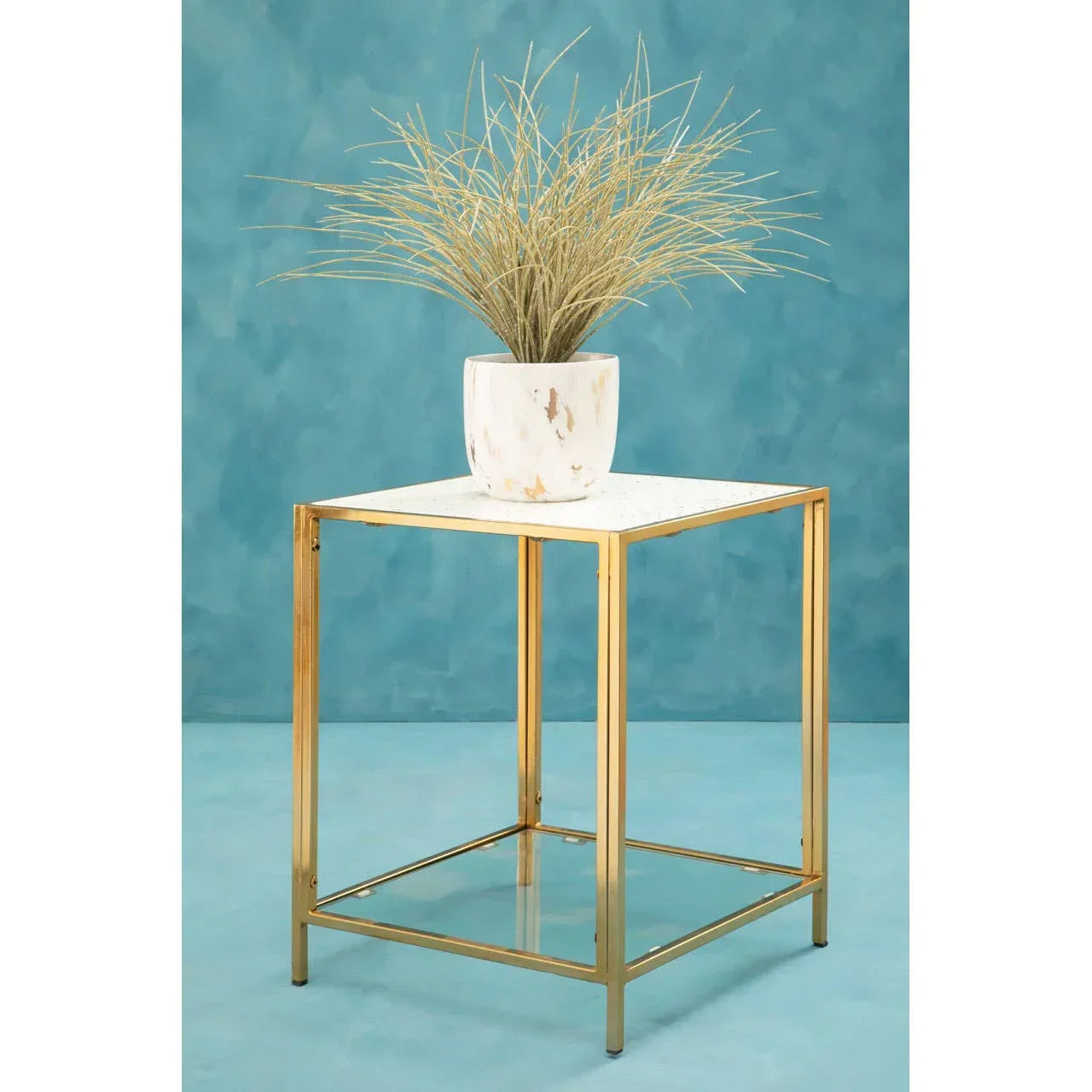 Gold metal side table with marble top and potted plant against a blue background