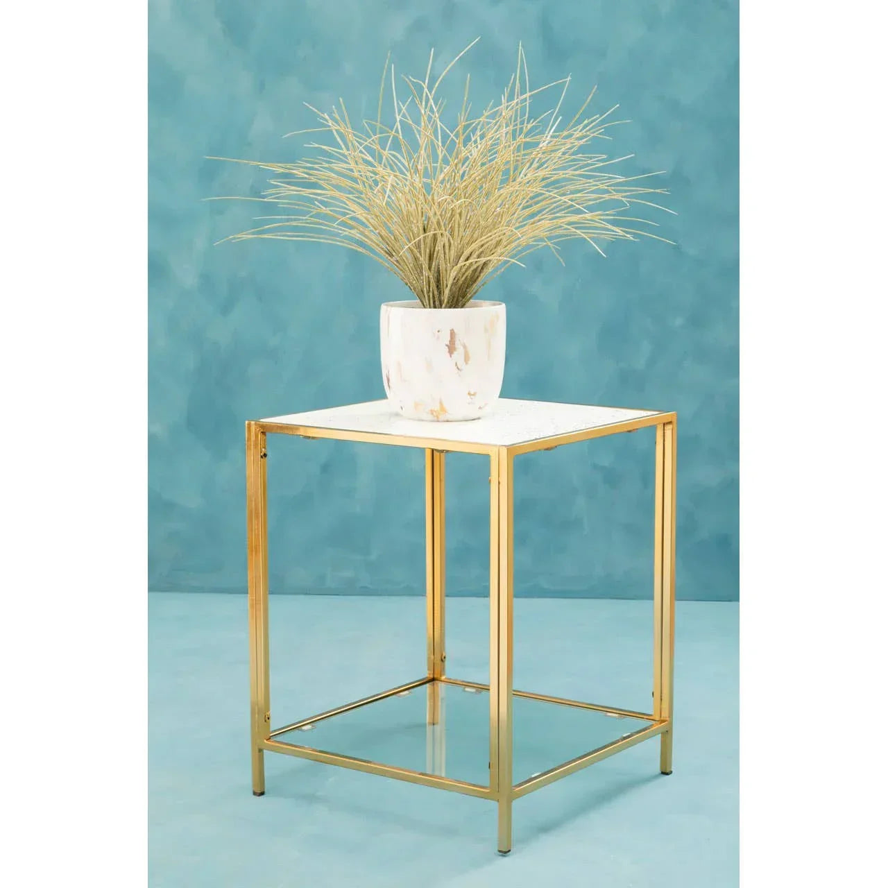 Gold metal side table with white marble top and potted plant against blue background