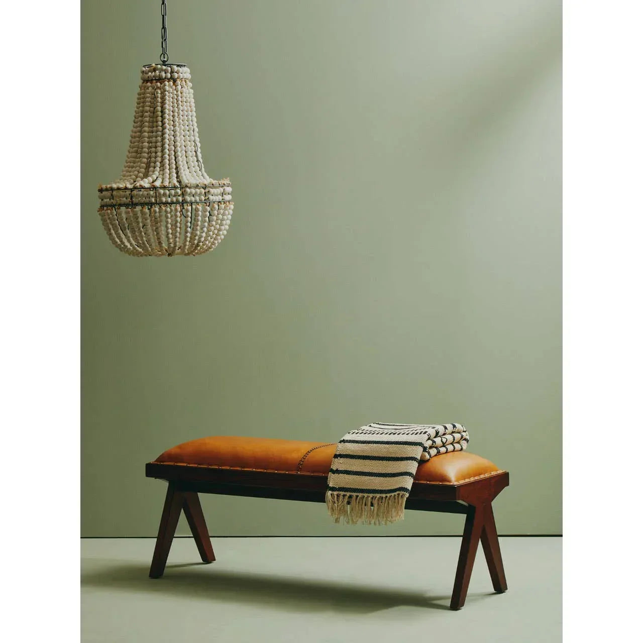 Tan leather bench with wooden legs and striped throw blanket under chandelier