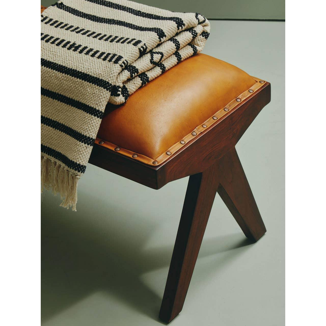Tan leather bench with wooden legs and striped throw blanket draped on top