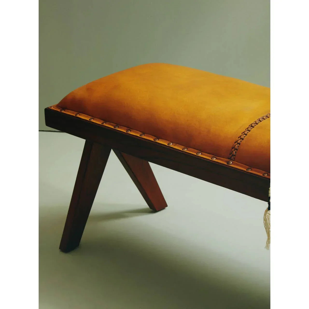 Mustard yellow upholstered bench seat with wooden legs and studded trim, side angle view