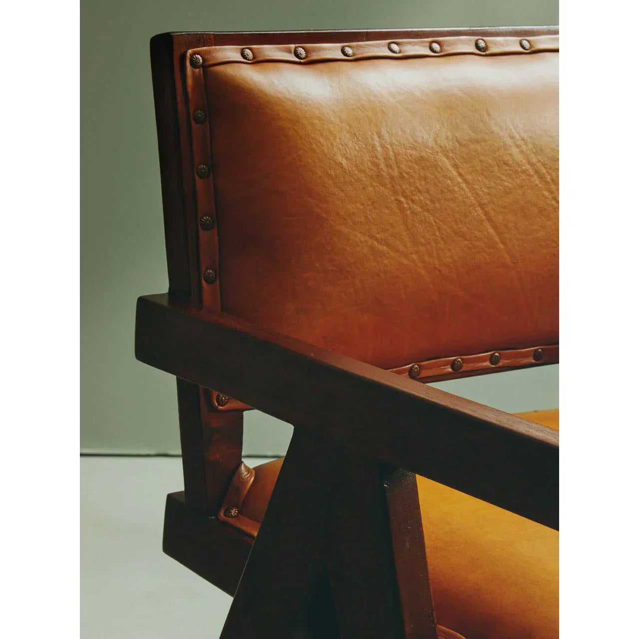 Brown leather armchair with studded detailing and wooden frame, side angle view