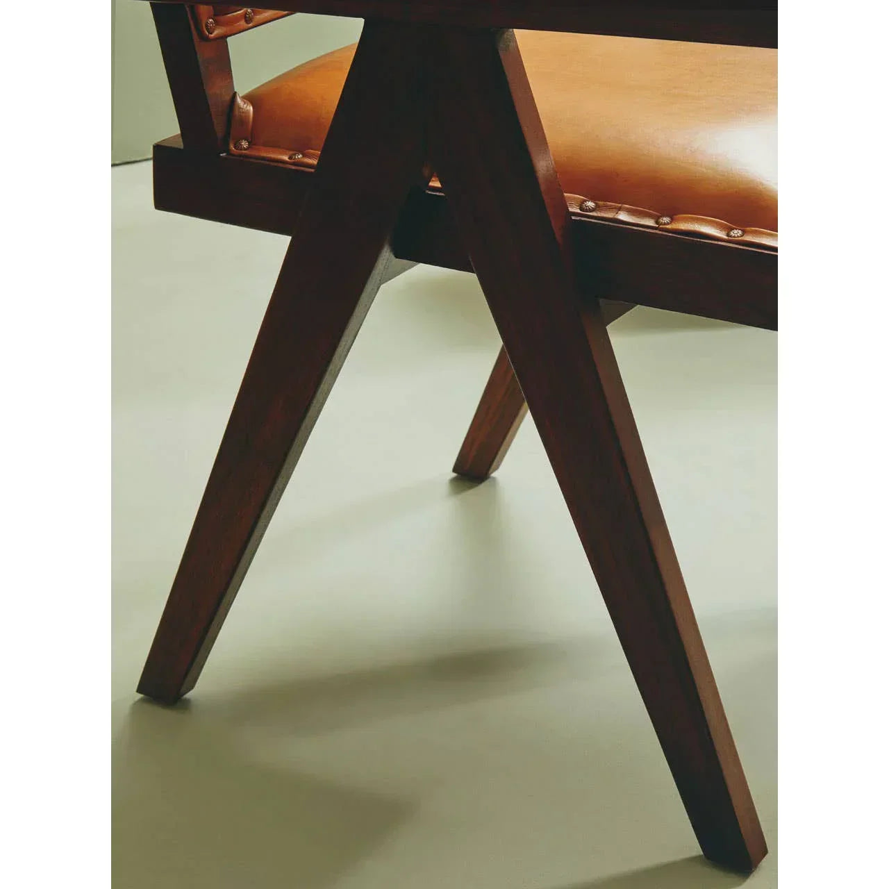 Close view of wooden dining chair legs and tan leather seat on light floor