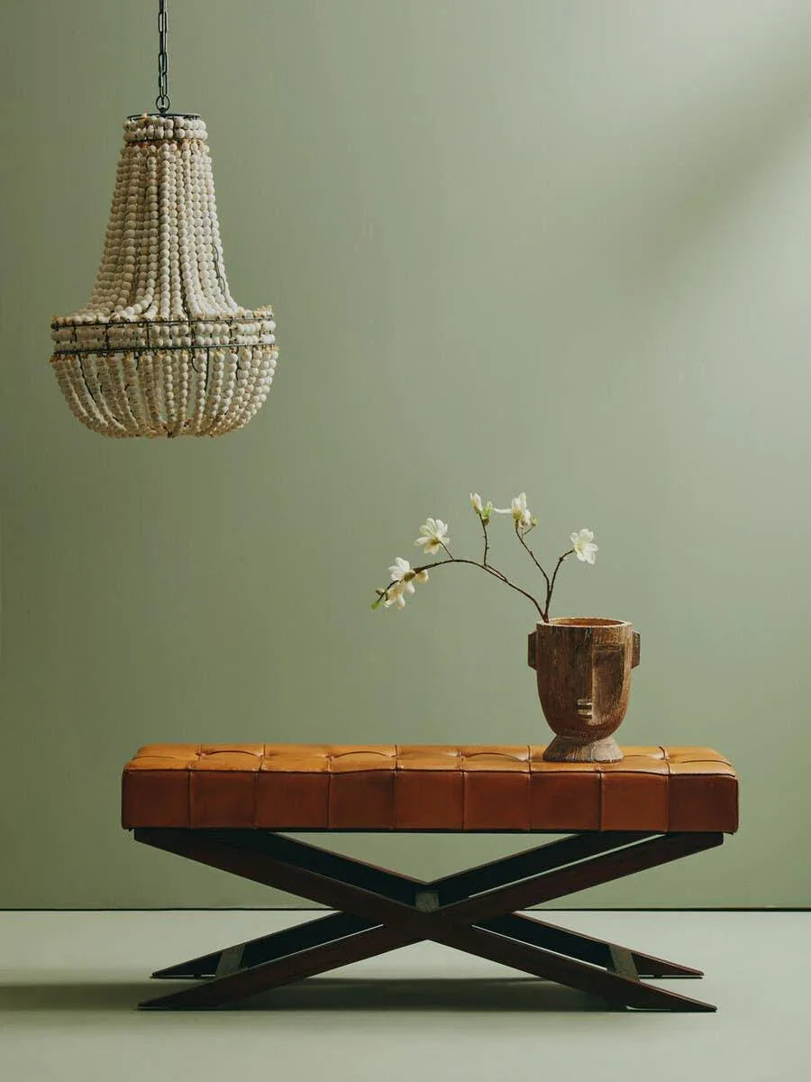 Brown leather bench with dark wood X-legs, decorative vase, and beaded chandelier