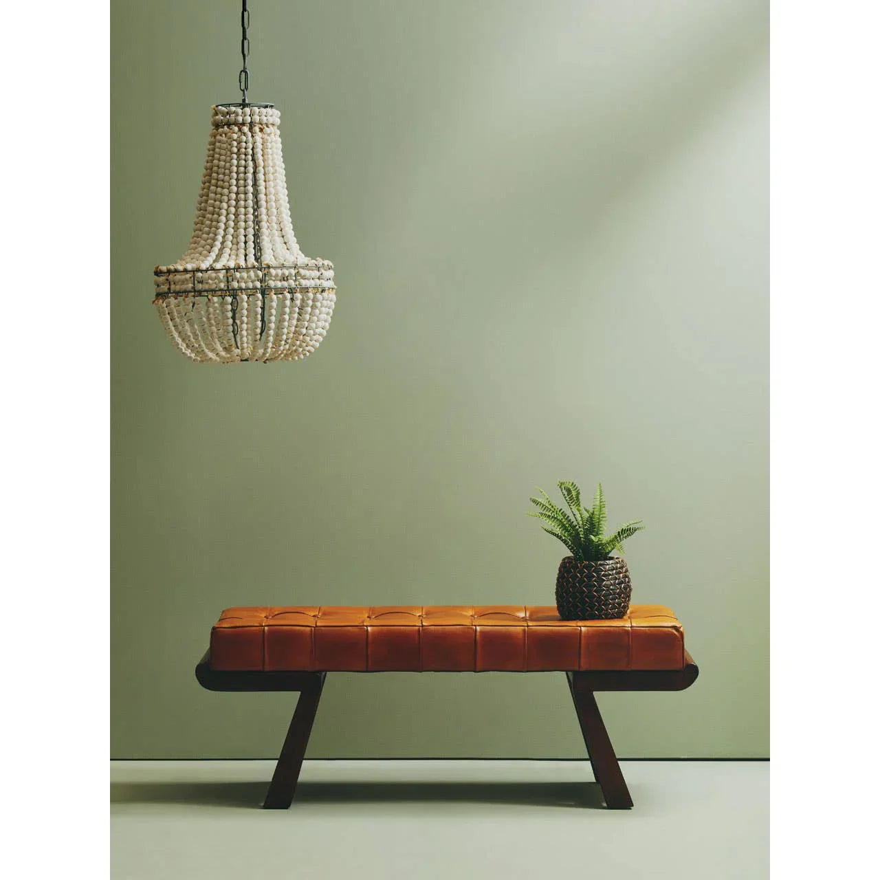 Brown leather bench with dark wooden legs, potted plant, and beaded chandelier