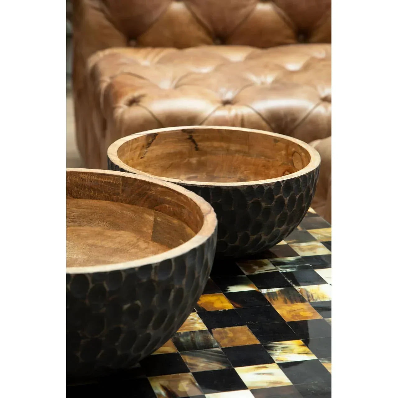 Textured wooden bowls on geometric inlay coffee table with leather sofa in background