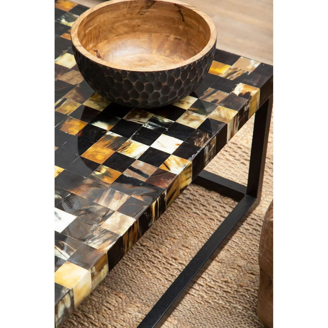 Checkered horn inlay coffee table with metal legs and wooden bowl on woven rug