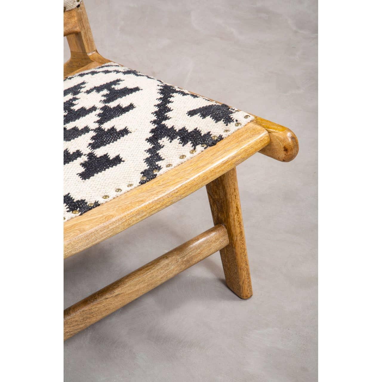Closeup of wooden chair with black and white patterned fabric seat on grey floor