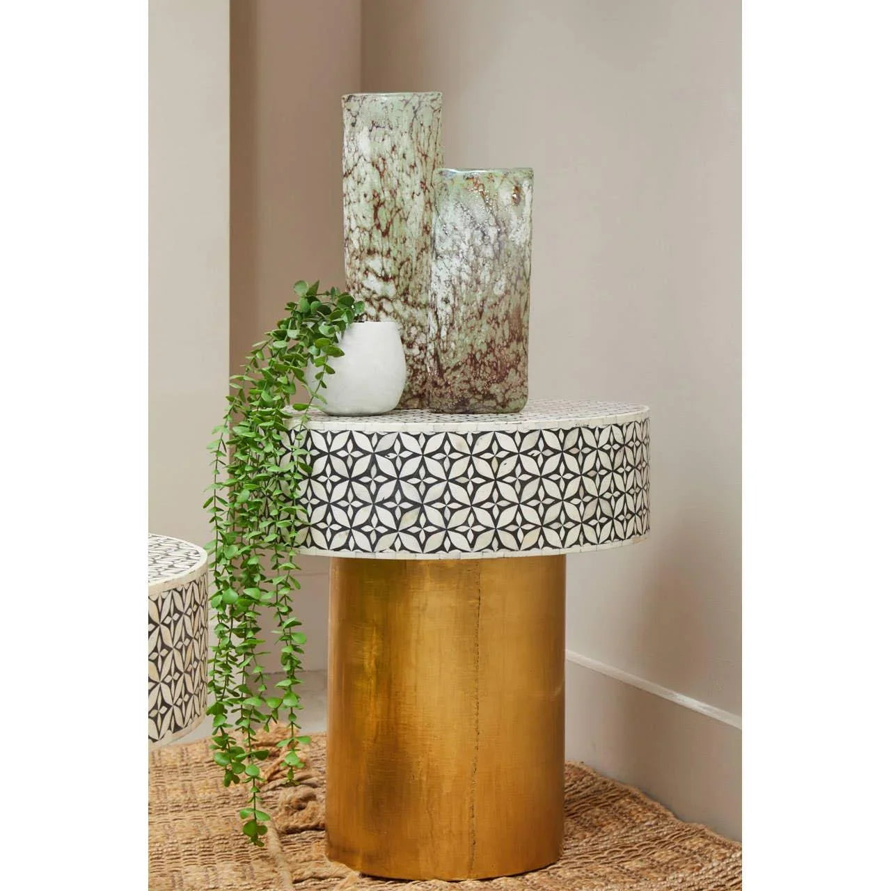 Round side table with patterned mosaic top and gold cylindrical base, vases and green plant