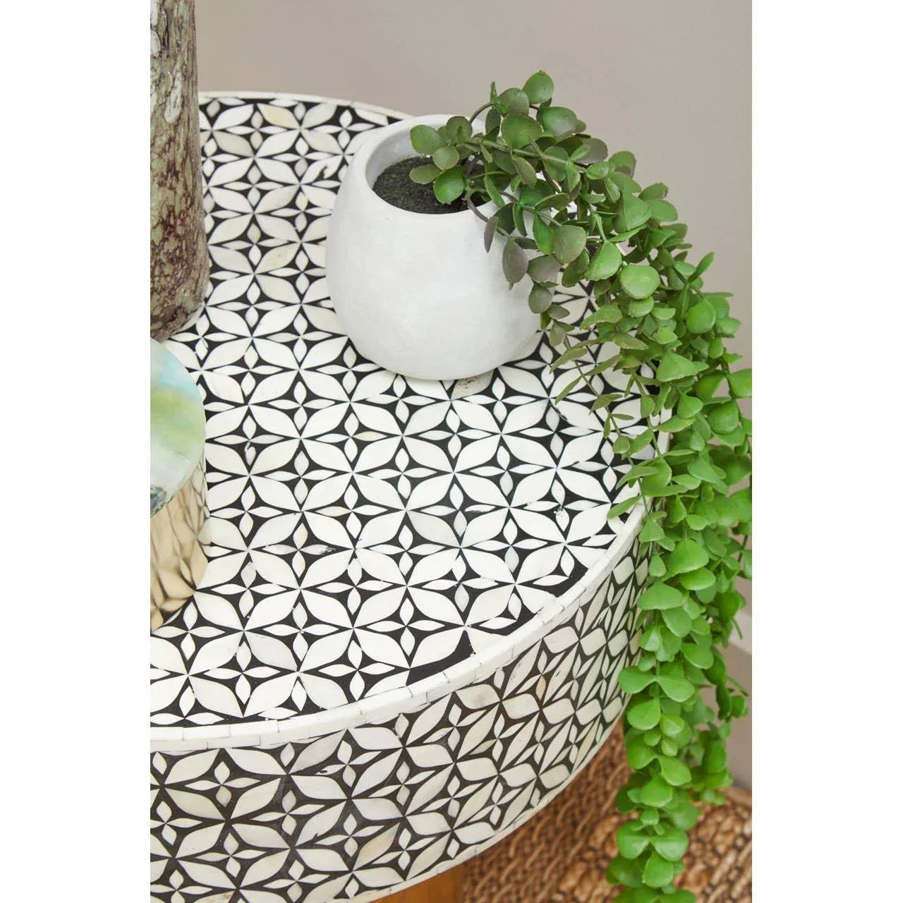 Round side table with black and white geometric pattern, small plant in white pot on top