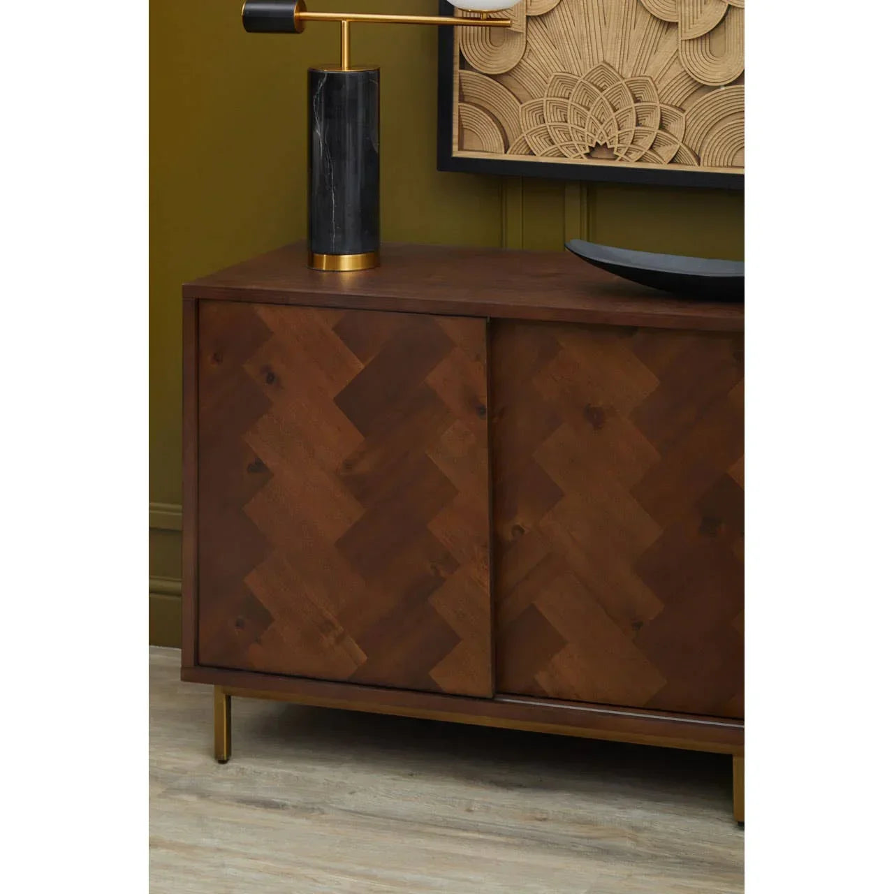 Walnut sideboard with herringbone wood doors and gold legs against green wall