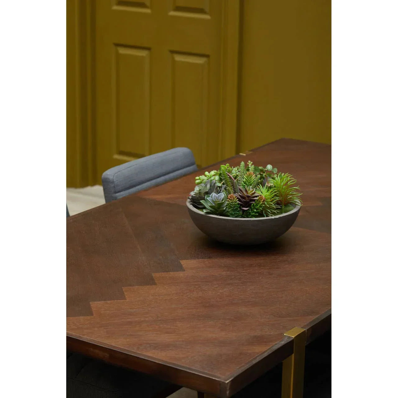 Rectangular wooden dining table with a bowl of artificial succulents and grey chair