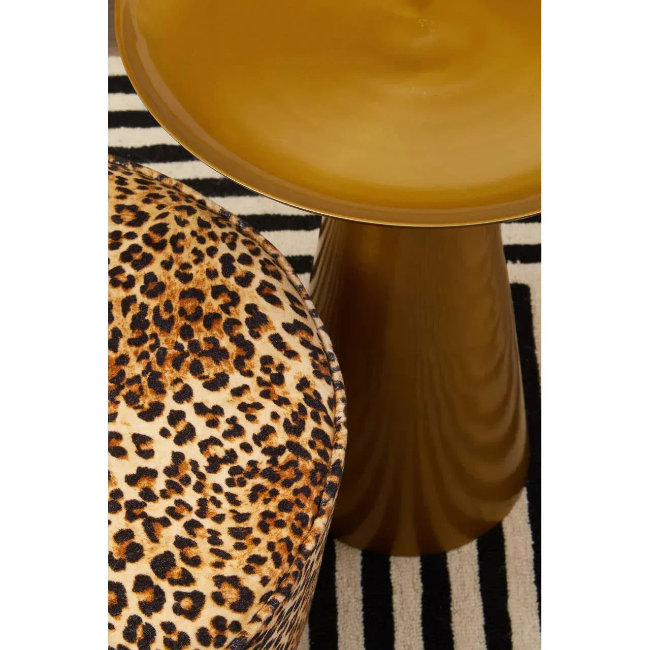 Leopard print ottoman beside gold metal side table on striped rug