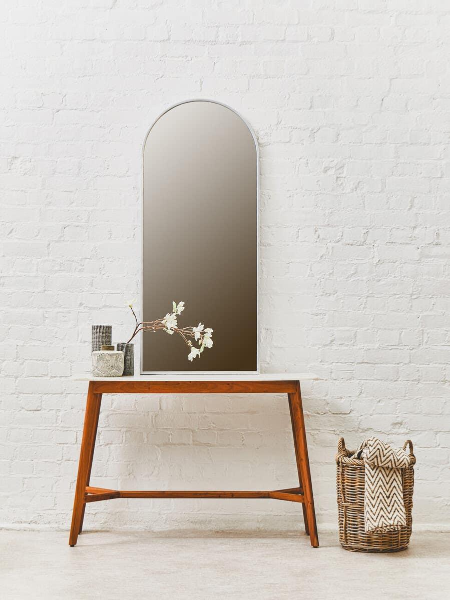 Arched wall mirror on wooden console table with woven basket and decorative vase