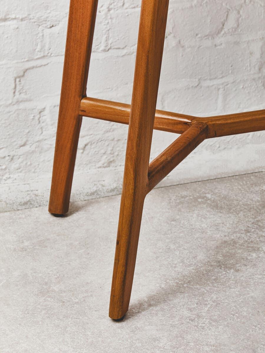 Wooden chair leg with natural finish on light concrete floor and white brick wall background