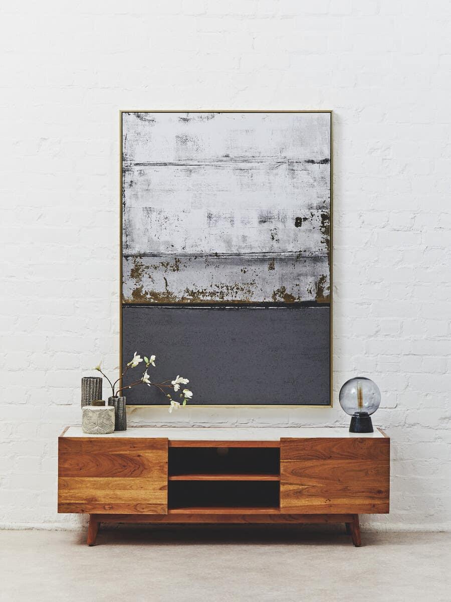 Wooden TV unit with open shelving, decorative vase, and table lamp against white brick wall