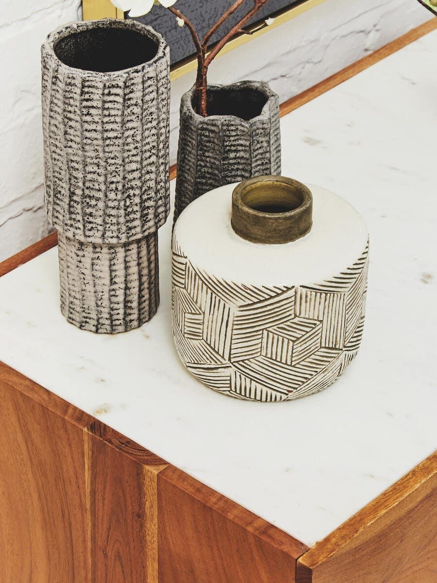 Textured ceramic vases and patterned round vase on white marble sideboard