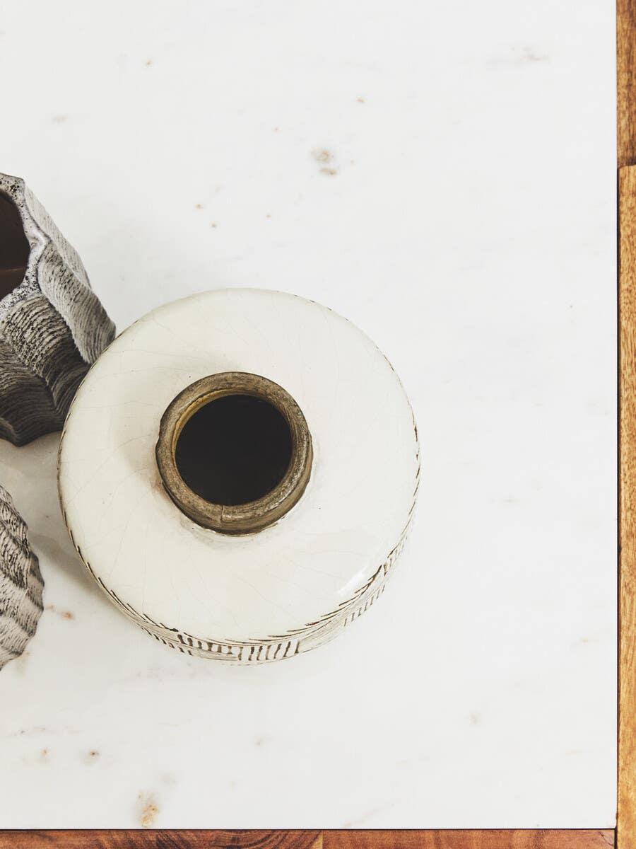 White ceramic vase on marble top beside textured grey decorative piece