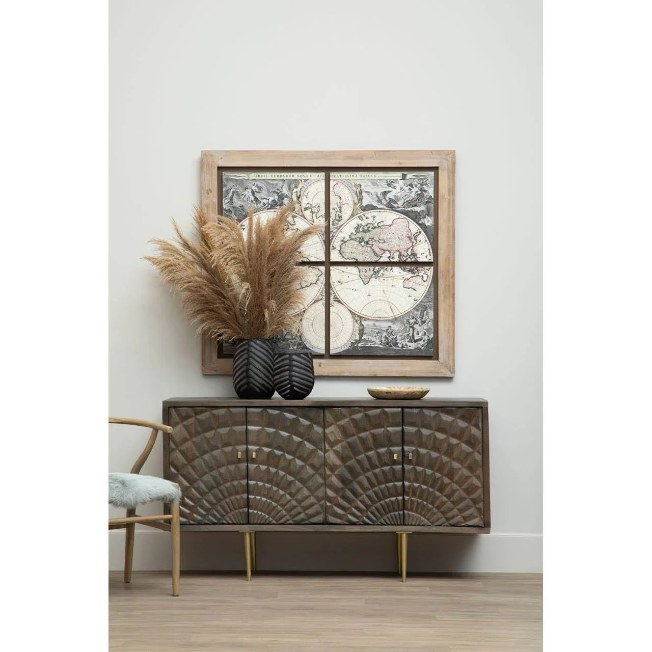 Wood sideboard with carved pattern, black vase with pampas grass, and framed map wall art