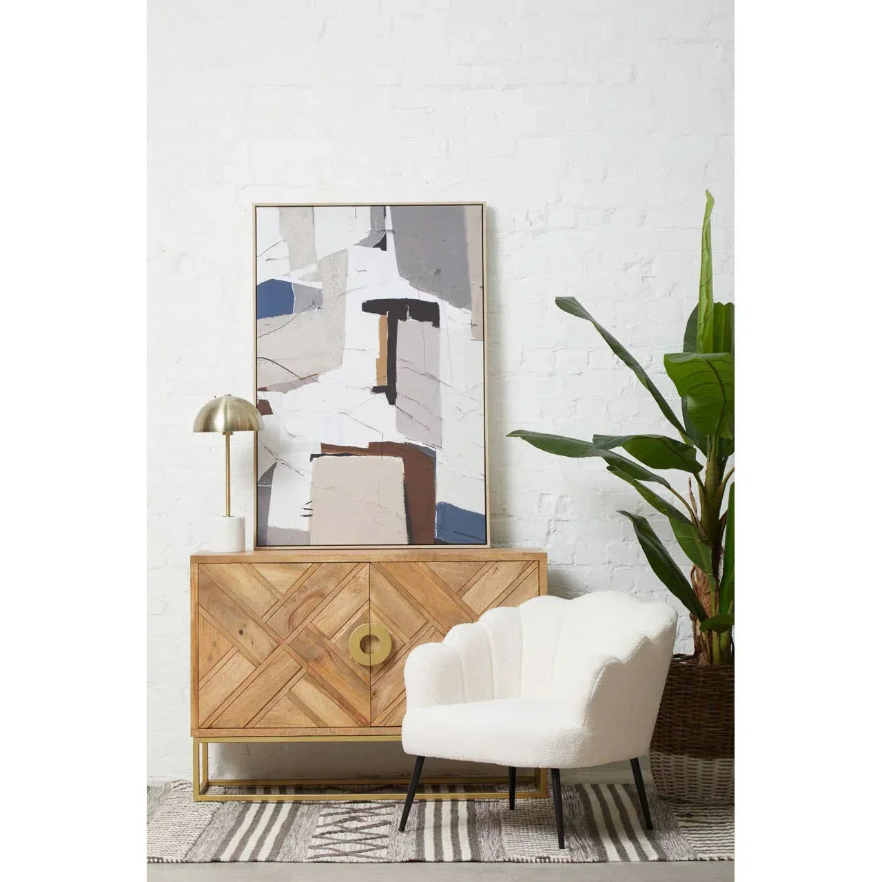 White scallop accent chair beside wooden sideboard and abstract wall art in modern living room