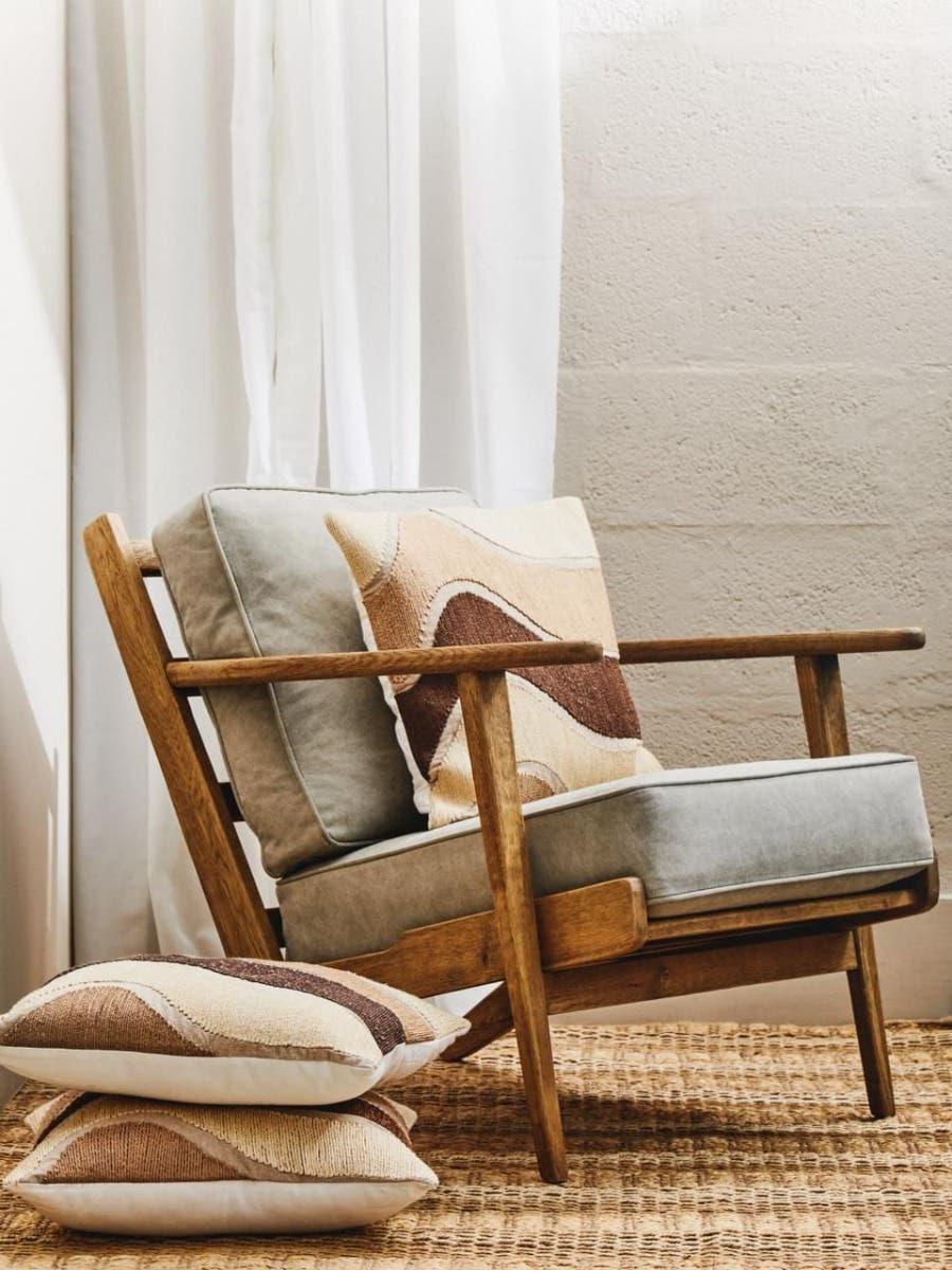 Wooden accent chair with light grey cushions and decorative pillows on woven rug