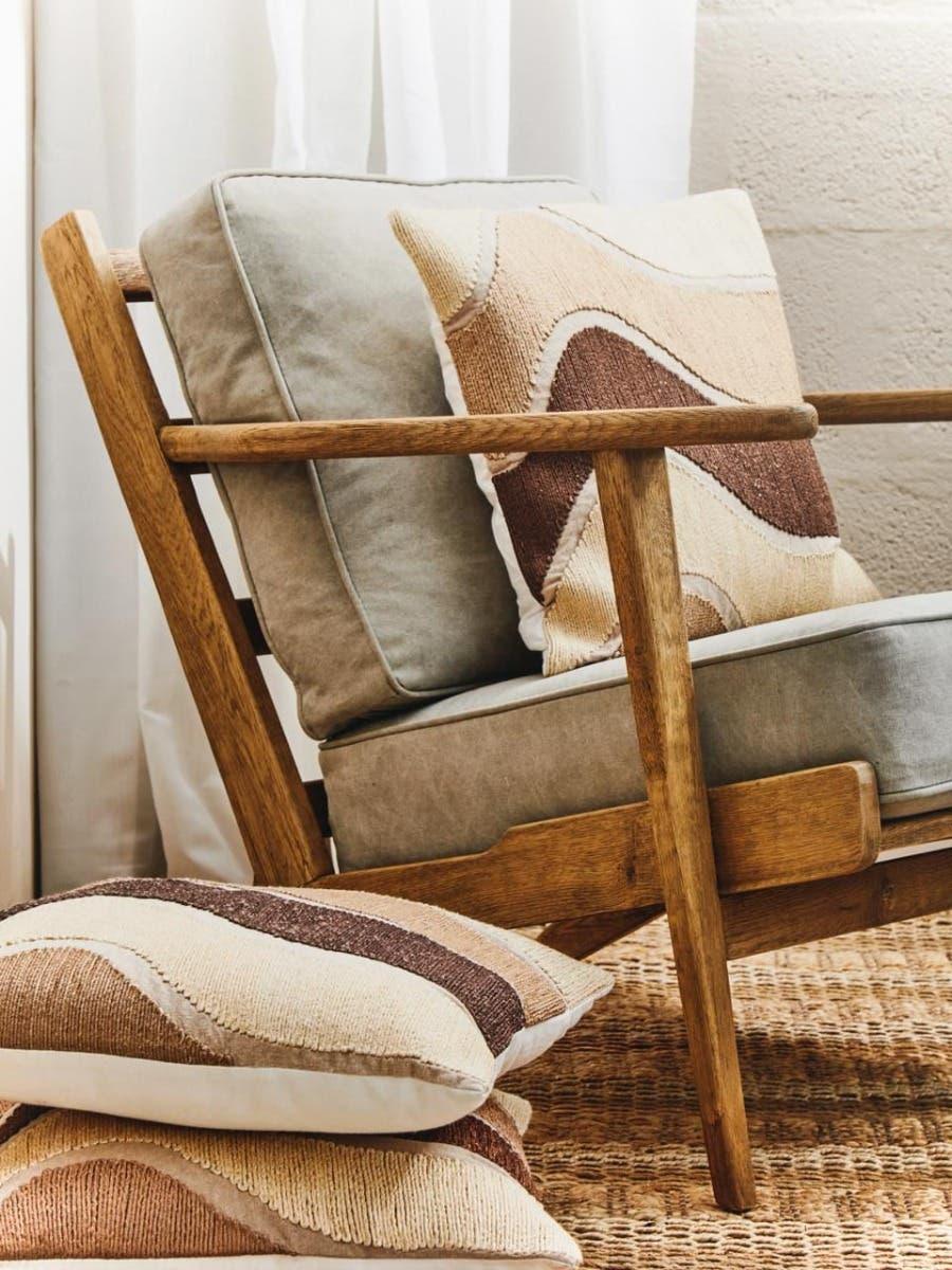 Wooden armchair with beige cushions and patterned throw pillows on a woven rug