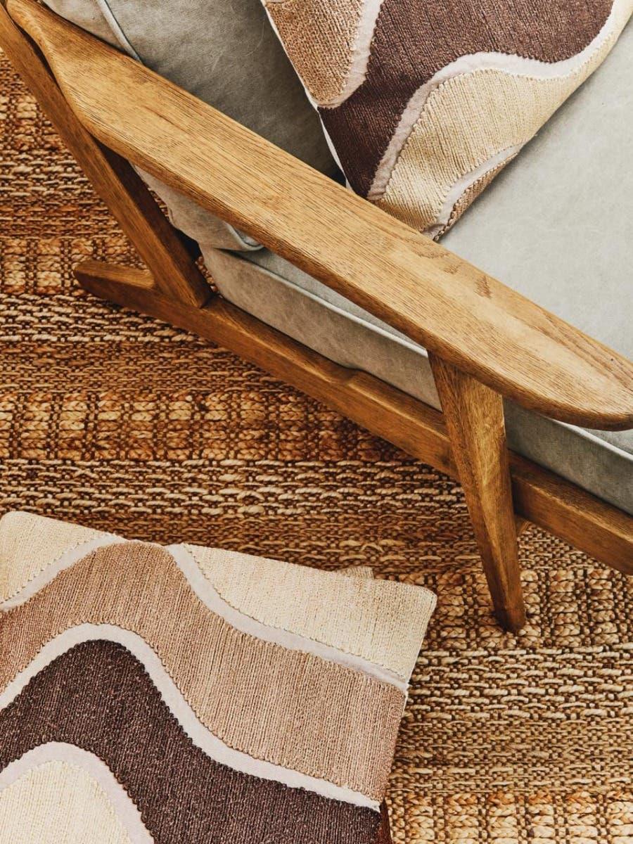 Wood armchair with beige upholstery, textured cushion and woven rug in neutral tones