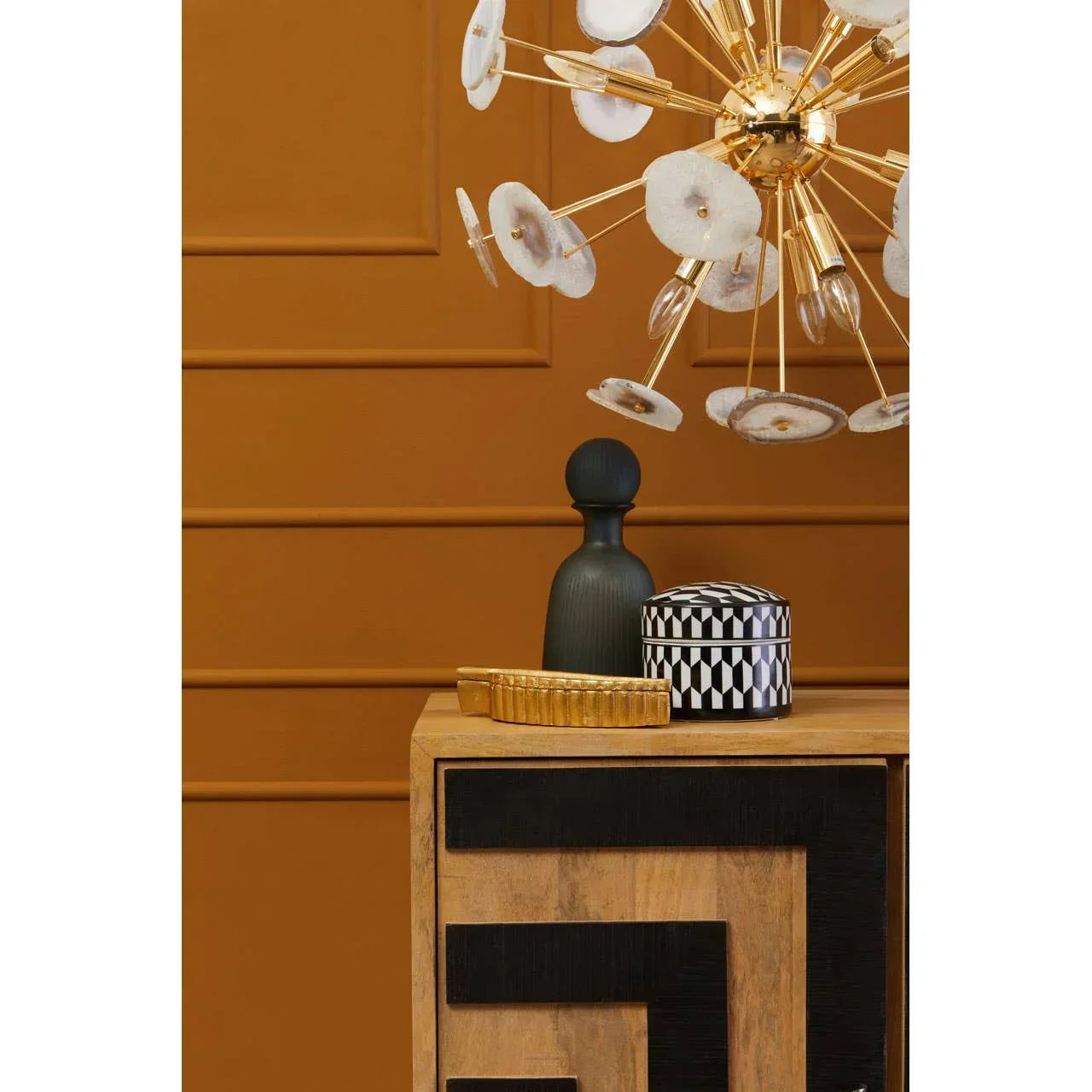 Wooden sideboard with black geometric detail and gold chandelier against ochre wall