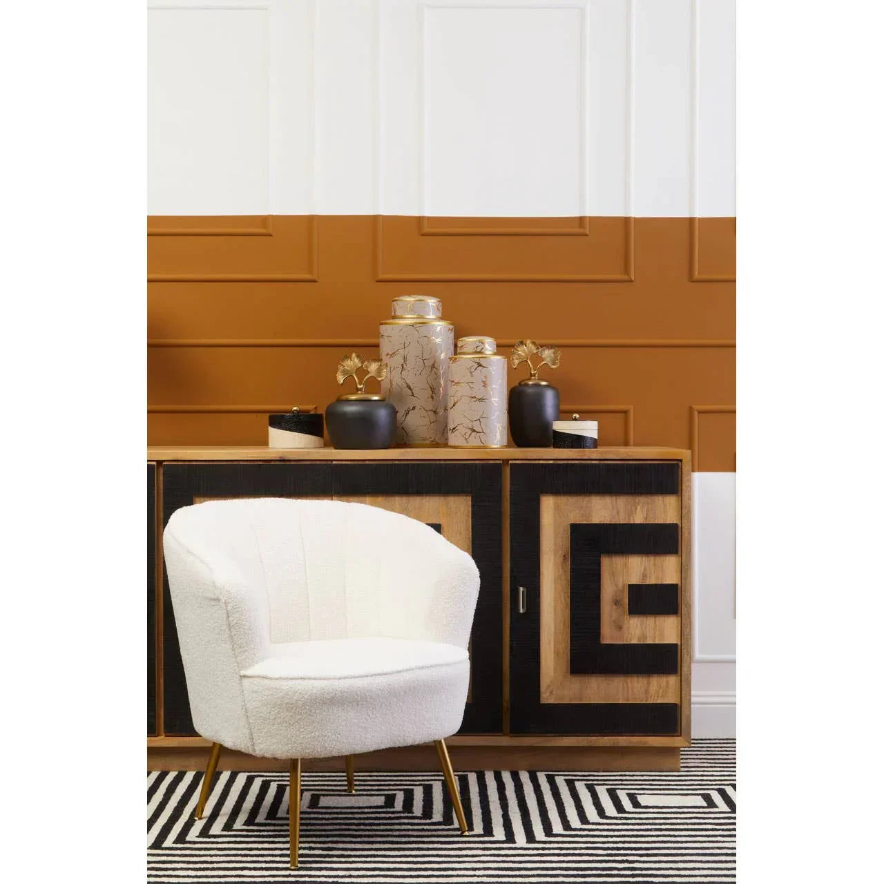 Modern accent chair with white upholstery and gold legs in front of geometric sideboard