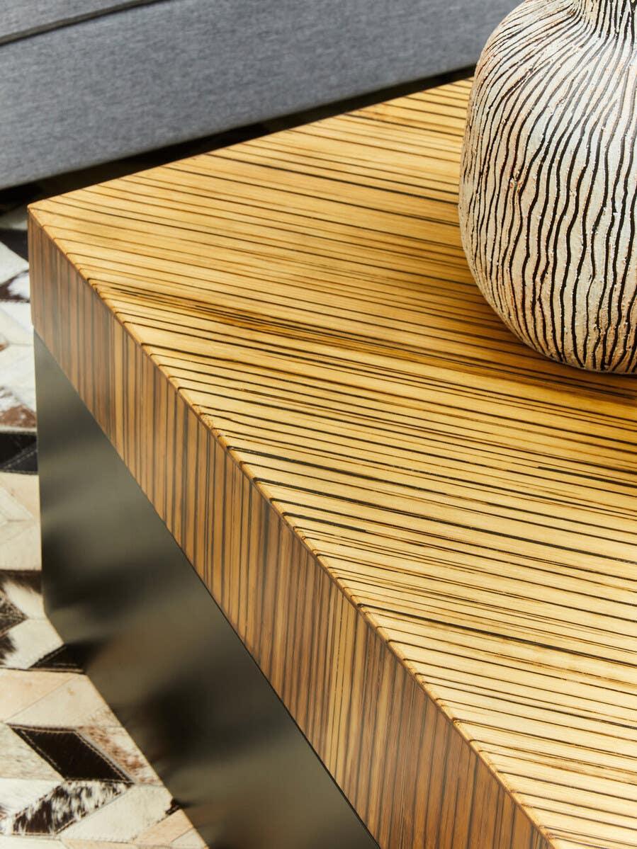 Zebrawood coffee table with striped veneer, decorative vase and patterned rug corner