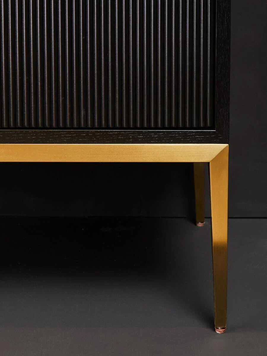 Black cabinet with ribbed doors and gold metal legs, close-up angle highlighting textures