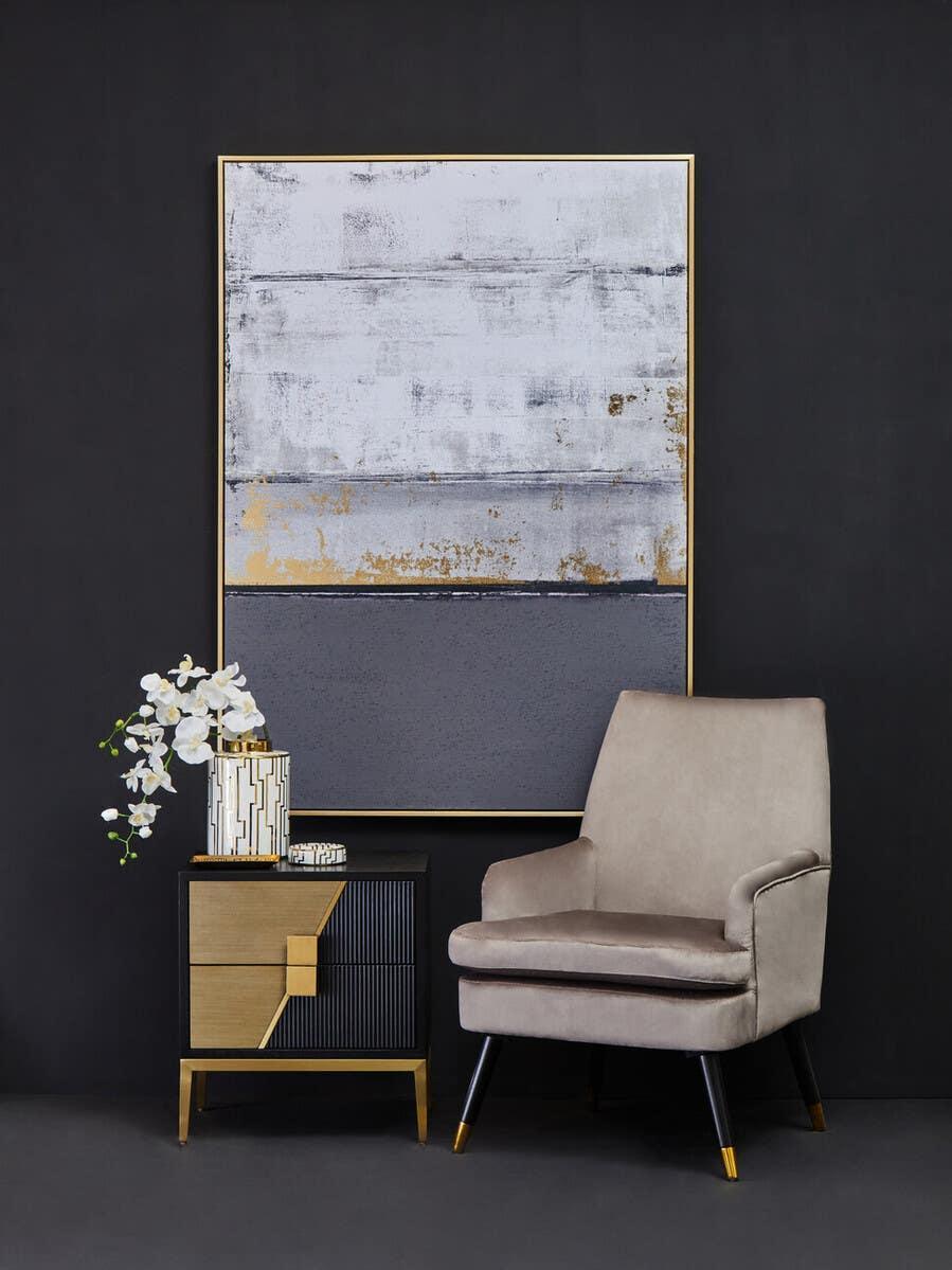 Modern beige accent chair beside black and gold bedside table with vase and abstract wall art