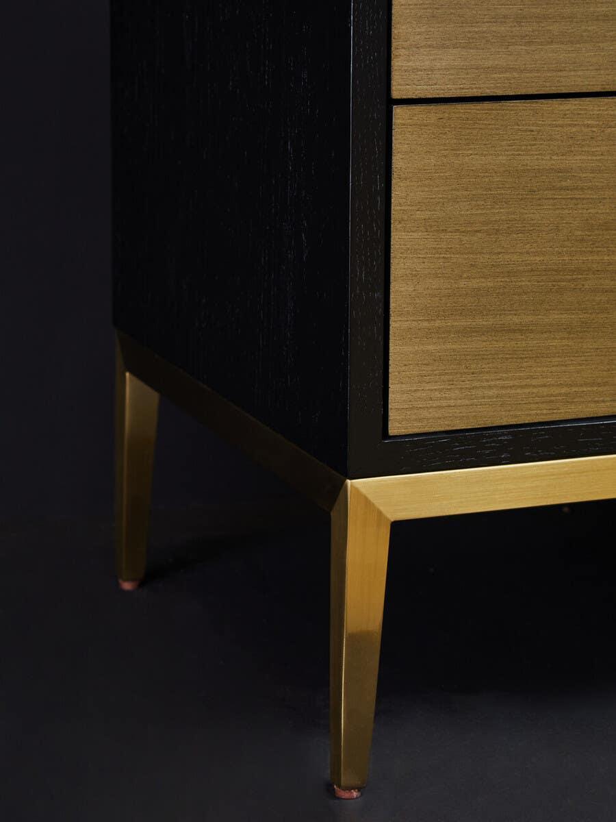 Closeup of wooden bedside table with brass legs and black frame against dark background