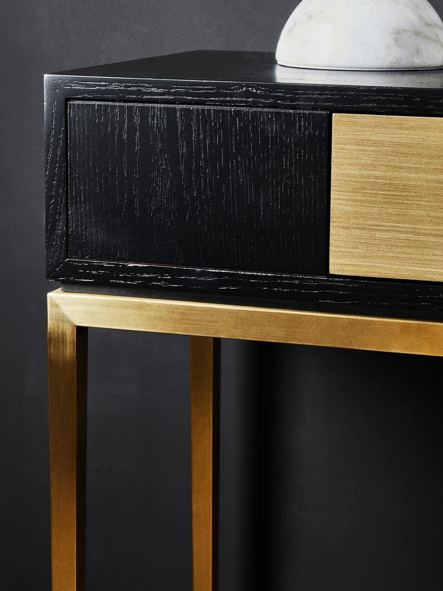 Black wood console table with gold metal frame and brass drawer detail, close-up view