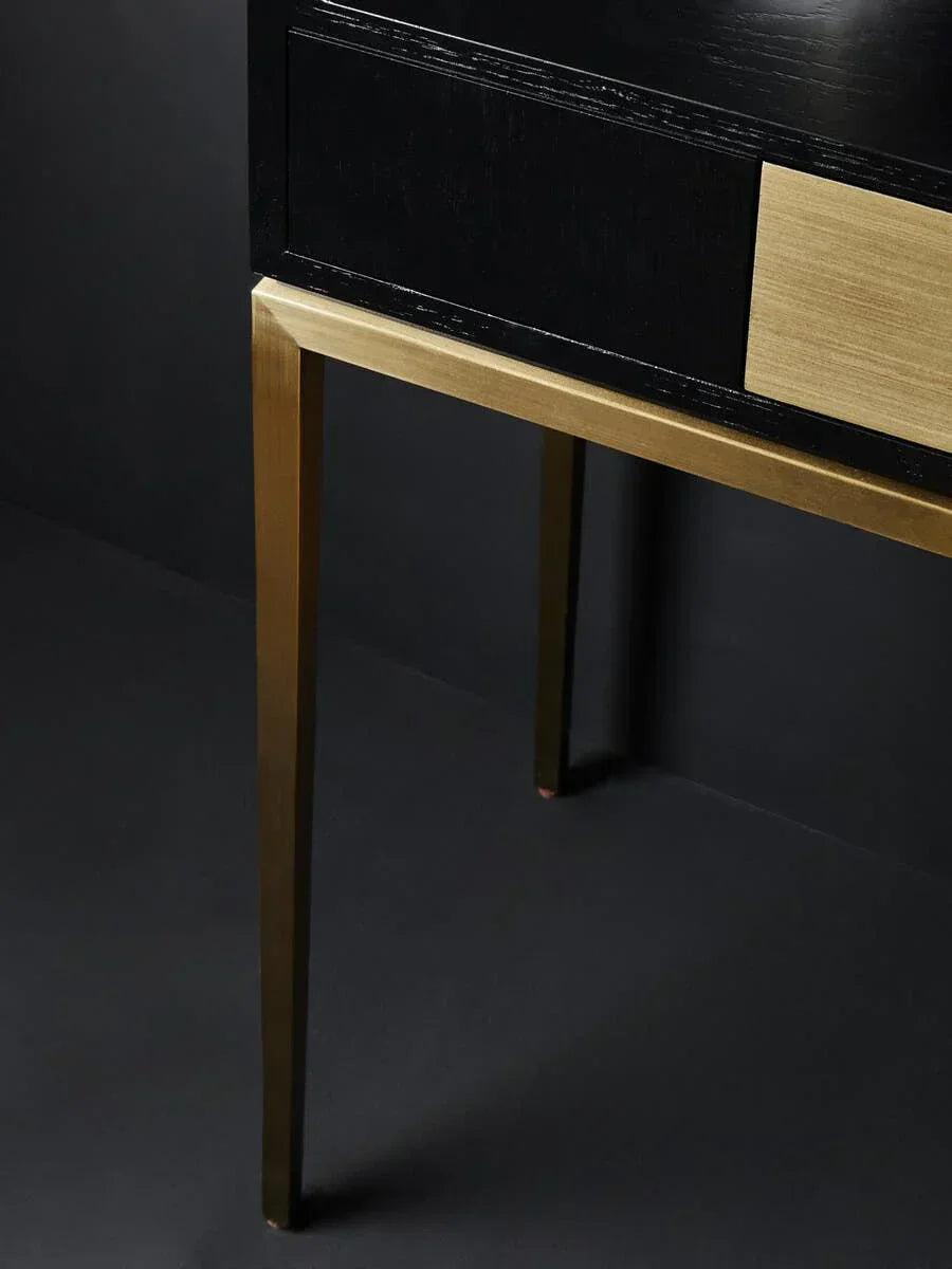 Black wood console table with brass legs and drawer front, close-up corner view