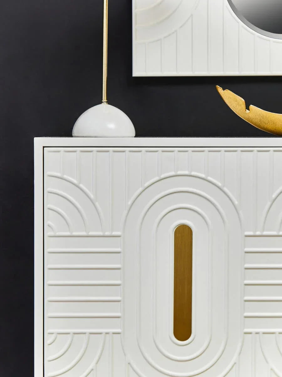 White sideboard with geometric carved doors and gold accents against black wall