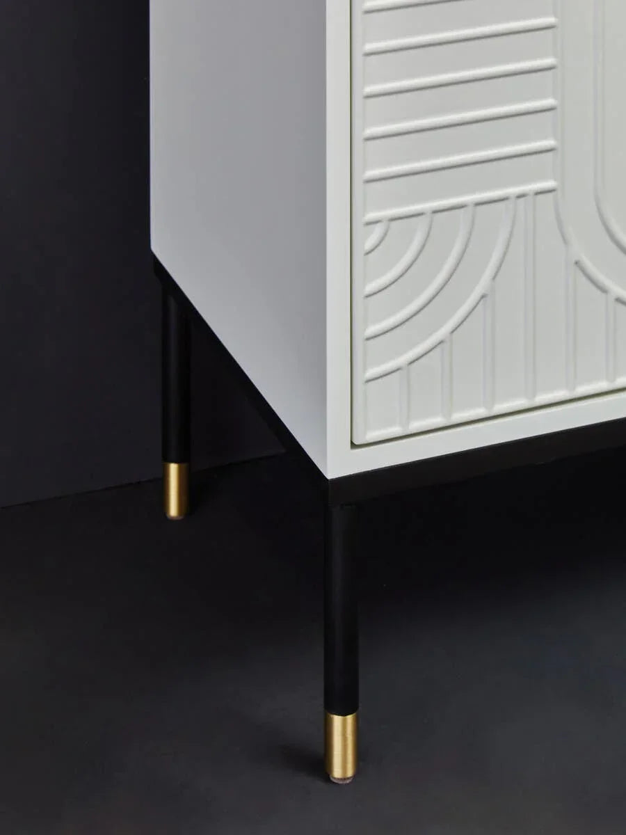 Close up of white cabinet with embossed doors and black legs with gold caps