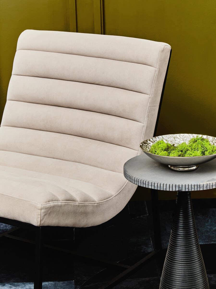 Beige velvet accent chair with horizontal stitching beside black modern side table and decor bowl