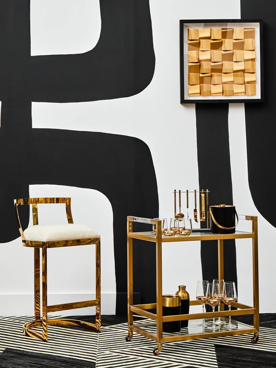 Gold bar cart with glassware and matching gold chair against black and white modern wall art