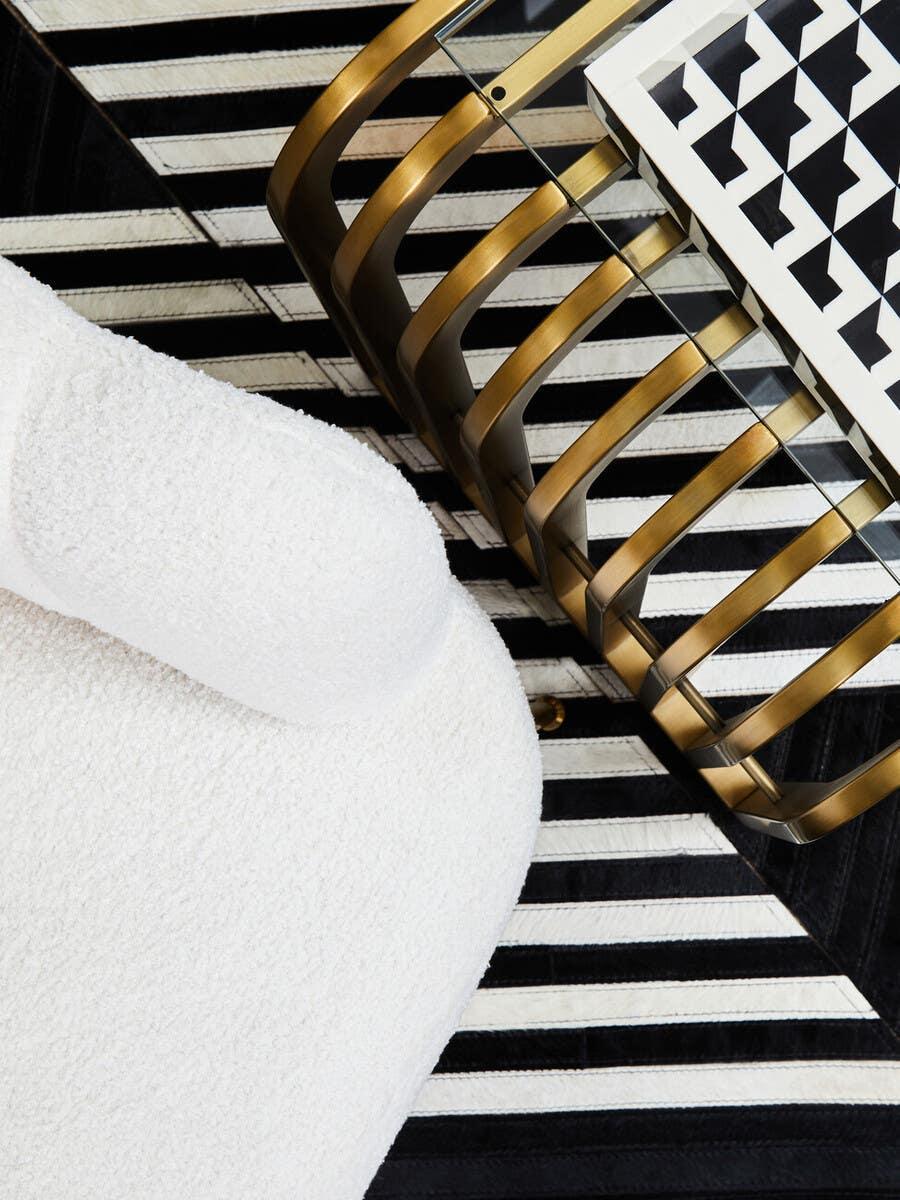Bouclé armchair next to gold frame glass coffee table on black and white striped rug