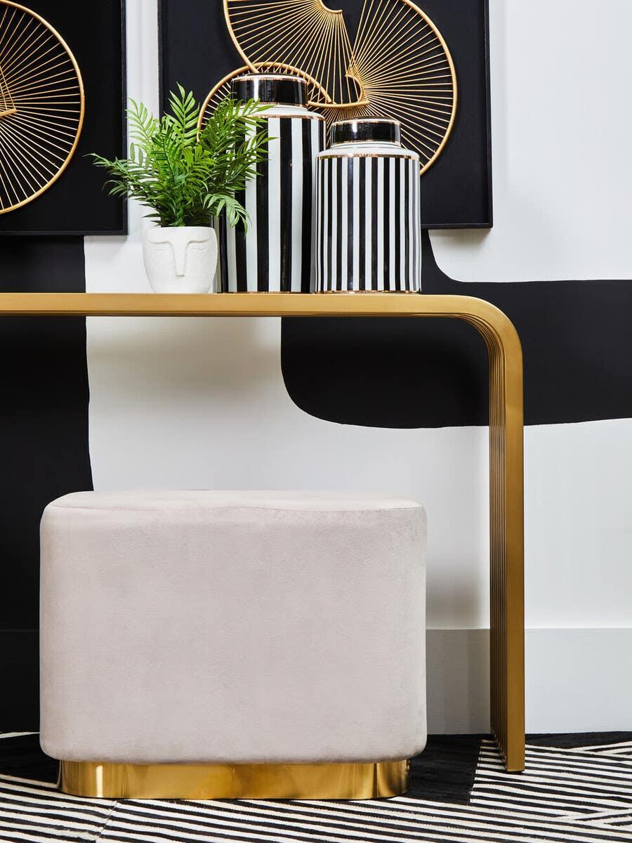 Beige velvet ottoman with gold base under gold-edged console table in modern hallway